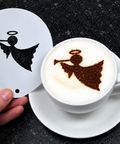A hand holds a white circular stencil with a black angel-and-brass instrument silhouette next to a white cup of latte art coffee on a saucer, showing the frothy coffee design created by the stencil.