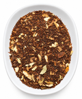 A top-down view of loose-leaf tea in a white oval dish against a white background. The tea consists of dark brown rooibos tea pieces with scattered light beige citrus peel flakes.