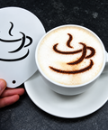 A hand holds a white ceramic coffee cup coaster with a black coffee cup graphic next to a white cup of cappuccino on a saucer, set against a dark textured background.