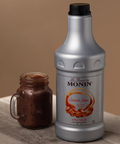 Bottle of Monin Caramel Sauce next to a jar of caramel sauce on a beige background