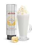 Monin white chocolate sauce bottle with a glass of white chocolate drink and white chocolate pieces on a white background