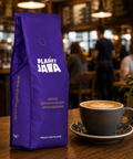 Purple Planet Java coffee bag with a cup of coffee on a wooden table in a café setting.