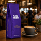 Purple Planet Java coffee bag with a cup of coffee on a wooden table in a café setting.