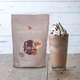 Sweetbird Mocha powder mix package next to a glass of mocha frappé with whipped cream on a wooden surface.
