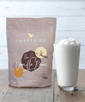 Sweetbird non-dairy vanilla bean product packaging with a glass of whipped cream on a wooden surface.
