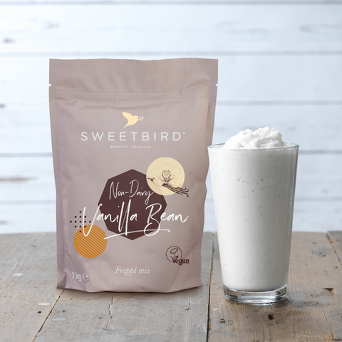 Sweetbird non-dairy vanilla bean product packaging with a glass of whipped cream on a wooden surface.