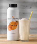 Sweetbird banana fruit juice bottle with a glass of banana smoothie on a wooden surface.