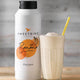 Sweetbird banana fruit juice bottle with a glass of banana smoothie on a wooden surface.