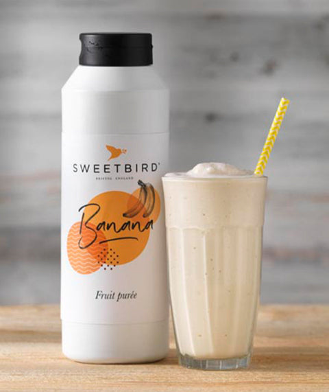 Sweetbird banana fruit juice bottle with a glass of banana smoothie on a wooden surface.