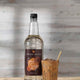 Bottle of Sweetbird Cane Syrup with a glass of iced coffee on a wooden surface.