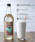 Sweetbird coconut syrup bottle with a glass of whipped cream and a straw on a wooden surface.