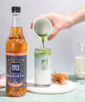 Tate & Lyle Barista Collection Caramel syrup being poured into a glass with ice and green liquid.