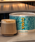 Zuma Vanilla Chai canister with a cup of coffee on a table in a cozy setting.
